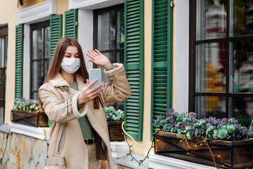 Fototapeta premium A young woman in a mask walks around the beautiful city and talks on the phone. holiday, christmas and health concept.