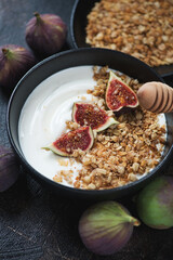 Close-up of greek yogurt served with granola, sliced figs and honey in a black bowl, vertical shot