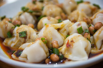 Close up of a traditional Tibetan dish: Stuffed dumplings in red sauce, with peanuts. Served in a white plate. Litang County, Garzê Tibetan Autonomous Prefecture, Sichuan, China 
