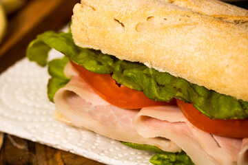 Ham, tomato and lettuce sandwich on a plate on a rustic background. Selective focus.
