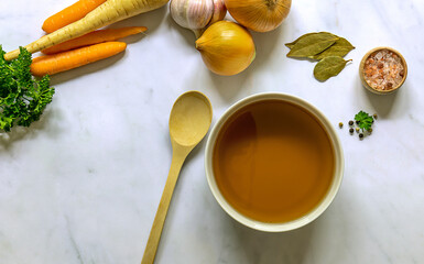 Flat lay of homemade beef bone broth in a bowl with ingredients. Contains minerals and healthy nutrients, including vitamins, amino acids, and essential fatty acids. 