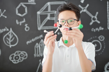 Pensive serious Asian student looking at chemical structure model
