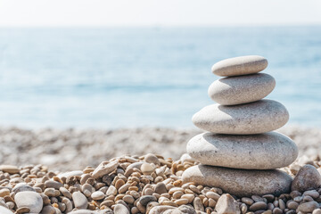 Fototapeta na wymiar Zen relax background. A pyramid of stones on the beach in clear sunny weather. Background for meditation, yoga and massage