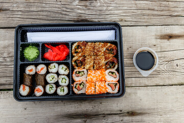 Set of sushi rolls in plastic box on wooden table. Sushi for take away or delivery of sushi in plastic container. Top view