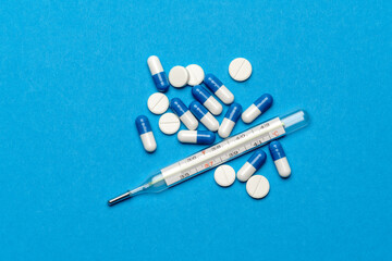 Fototapeta na wymiar group of white pills or tablets and mercury thermometer on blue background