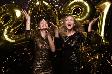 Happy gorgeous girls in stylish sexy party dresses holding gold 2021 balloons, having fun at New...