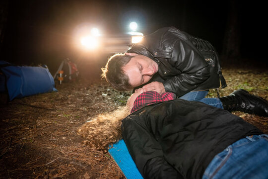 A man determines if a woman lying on the ground is breathing. Field training in first aid. Headlights scene, selective focus.