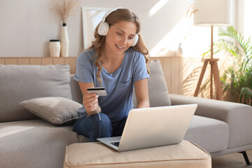 Happy natural blonde using credit card and laptop in the living room.