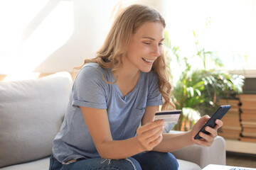 Happy natural blonde using credit card and mobile phone in living room.