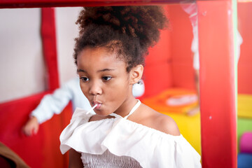 Portrait of adorable African American girl kid with curly hair eating sweet candy, joyful child enjoy with her snack
