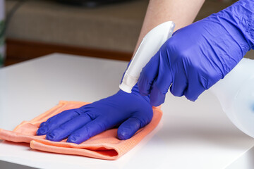 Young woman in medical purple gloves disinfecting the table surface with sanitizing antibacterial wipes. Protection against COVID-19. Concept of surface disinfection in hospitals and public places