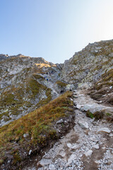 Many tourists climbing steep trail with chains towards Szpiglasowa Pass in Tatra Mountains, Poland, autumn.