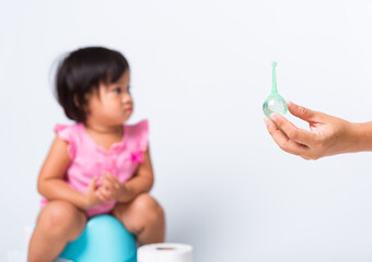 Asian little cute baby child girl training to sitting on blue chamber pot or potty her problem cannot shit and mother use Enema for help, studio shot isolated on white background, wc toilet concept