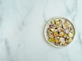 Waldorf salad with copy space. American fruit and nut salad with apples, celery, grapes, chicken meat, dressed mayonnaise. Craft plate with ready-to-eat waldorf salad on white marble. Top view