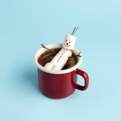 Winter layout made with red mug with hot chocolate and melted marshmallow snowman on blue...