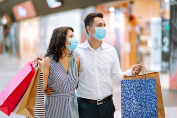 Portrait of a couple with shopping bags in protective sterile medical mask in mall. Shopping in the coronavirus pandemic. People, sale, love, black friday and happiness concept.