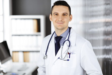 Male doctor standing straight in clinic near his working place. Perfect medical service in hospital. Medicine and healthcare concept