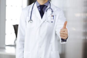 Unknown male doctor standing with thumbs up sign in clinic near his working place, closeup. Perfect medical service in hospital. Medicine and healthcare concept