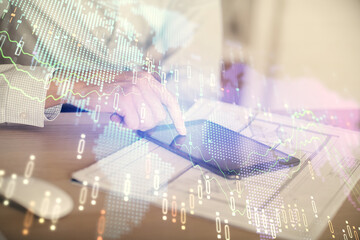 Double exposure of man's hands holding and using a digital device and forex graph drawing. Financial market concept.