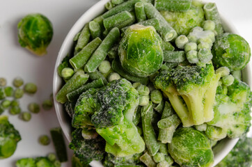 A mix of frozen green vegetables: beans peas broccoli Brussels sprouts in bowl on white