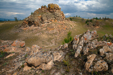 Beautiful colorful contrast landscape with hills and textured rock stones, mountain valley in sunshine on dramatic cloudy sky background, Russia, lake Baikal region