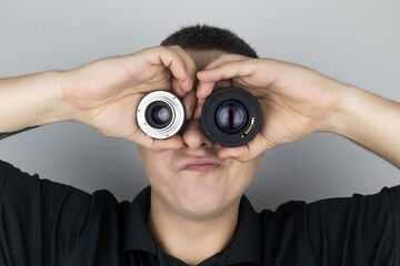 A man tries on two camera lenses instead of eyes. He plays around and fools around. The concept of the photographer's work and the creative approach to photography