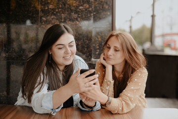 Two young women sit in an open cafe in the city with a phone