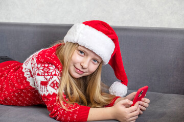 Little girl in Santa's hat talking to phone.