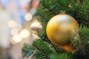 Close up view on a gilded ball on the  Christmas tree on a background of glow lights in bokeh (shallow depth of field)