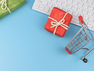 flat lay of red and green gift boxes with computer keyboard and shopping cart on blue background with copy space. Online shopping and Christmas holiday concept.