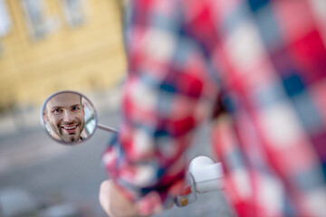 Man looking at his scooters looking at the rear-view mirror