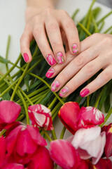 Female hands with spring manicure and tulips nail art, floral design on flowers background. Beauty, fingernails and hands care concept. Vertical shot.