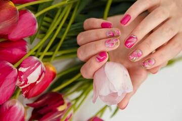 Female hands with tender spring manicure holding pink fresh tulip on flowers background. Nail art, gel nails polish design and beauty concept.
