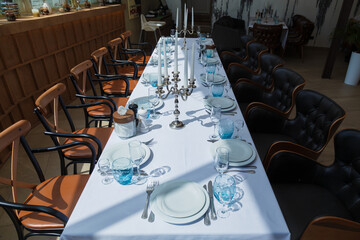 Festive table set with white cloth, plates, forks blue glasses and candlestick with white candles for wedding, family event or happy birthday party.