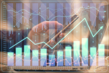 Double exposure of man's hands holding and using a phone and financial graph drawing. Analysis...