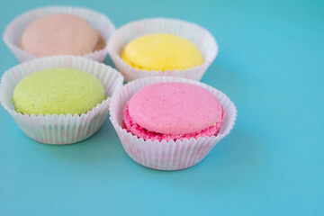 Multi colored french almond macarons in white paper baking molds on blue background with copy space