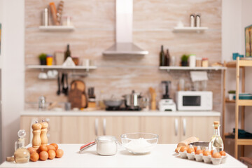 Pastry ingredients for homemade cakes and bread in empty kitchen. Modern dining room equipped with utensils ready for cooking with wheat flour in glass bowl and fresh eggs on table