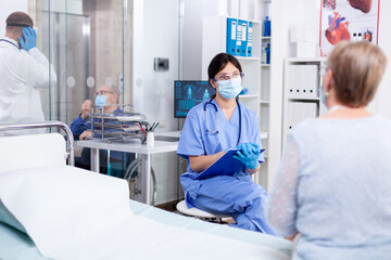 Obraz premium Medical staff wearing protective mask against coronavirus pandemic and talking with senior patient during consultation in medical examination room. Practitioner physician appointment