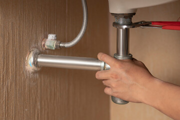 Plumber repairs and maintains chrome siphon under the washbasin in bathroom. Maintanance home ideas concept. Selective focus and freespace for background.