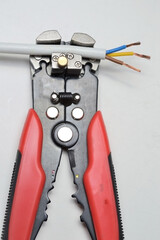 a wire stripper and a protected three-core wire on a white background. close-up