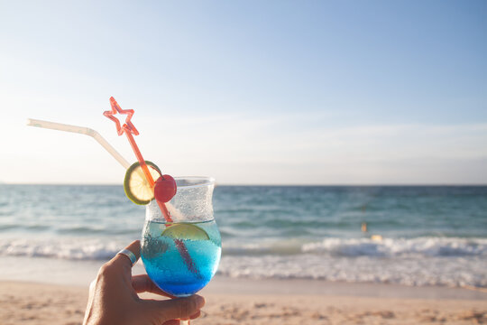 Woman's hand holding glass of summer drink with beach on background