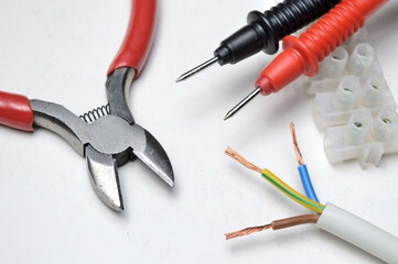 cutters, electric wire, tester probes and terminal block on a white background close-up.