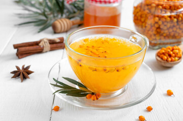 Colorful hot natural sea buckthorn tea in a glass cup, fresh raw berries and leaves, honey, anise and cinnamon sticks. Vitaminic healthy medicine drink. Concept of warm seasonal beverages.