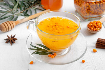 Colorful hot natural sea buckthorn tea in a glass cup, fresh raw berries and leaves, honey, anise and cinnamon sticks. Vitaminic healthy medicine drink. Concept of warm seasonal beverages.