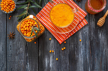 Colorful hot natural sea buckthorn tea in a glass cup, fresh raw berries and leaves, honey, anise and cinnamon sticks. Vitaminic healthy medicine drink. Concept of warm seasonal beverages.