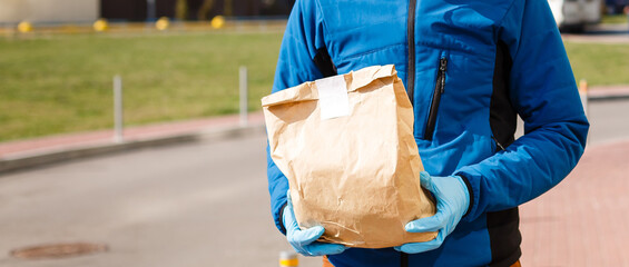 Delivery man holding paper bag with food, food delivery man in protective mask