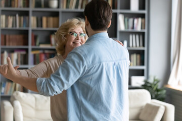 Back rear view affectionate caring young man leading in slow dance smiling middle aged 60s senior...