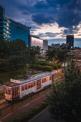 Obraz premium Old tram passing at sunset near Piazza Gae Aulenti in the new and modern district of Porta Nuova in Milan. Sky with clouds