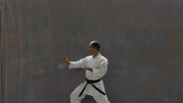 Young sportsman with blue belt doing formal exercises against the background of a street wall