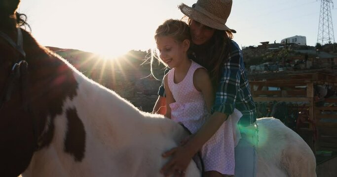 Happy mother and daughter riding a horse at sunset - Family and love concept